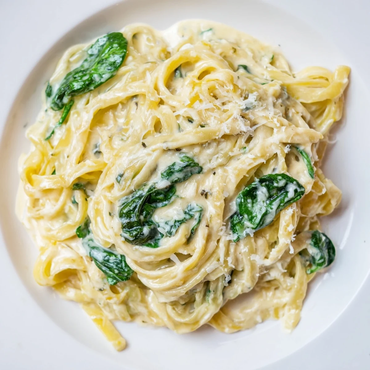 Steaming creamy garlic spinach pasta in a skillet, featuring wilted green spinach leaves and golden garlic pieces.