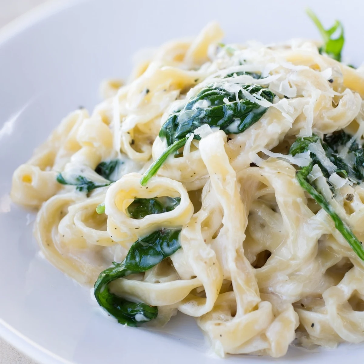 Freshly plated creamy garlic spinach pasta, served alongside a glass of white wine on a rustic wooden table.