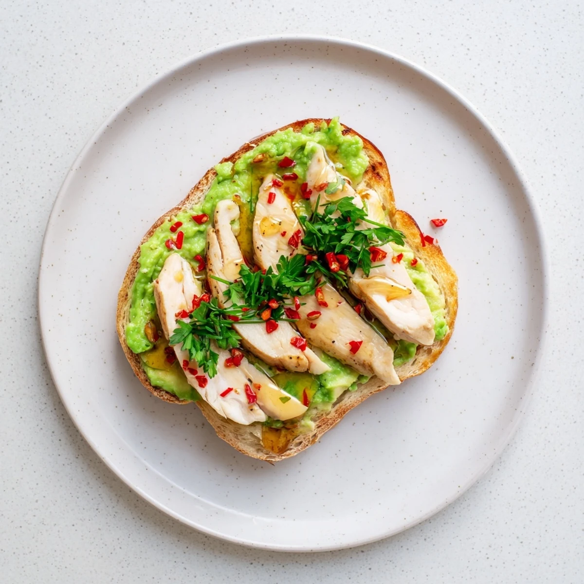 A close-up shows hand-mashing ripe avocado with lemon juice onto rustic bread, adding smoky paprika-seasoned grilled chicken slices for a savory-sweet bite.