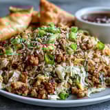 Fork scooping up savory Crispy Chicken Fried Rice with Egg Roll Flavors, featuring crunchy cabbage, carrots, and fluffy rice.