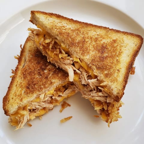 A close-up of a juicy Crispy Shallot Chicken Grilled Cheese with melted mozzarella and toasted sourdough bread.