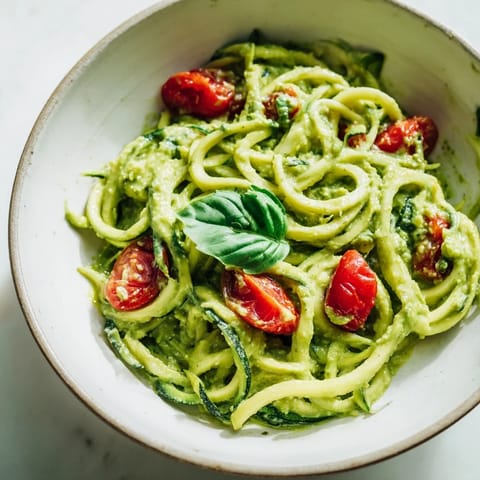Creamy avocado pesto zoodles topped with halved cherry tomatoes in a vibrant green bowl.  