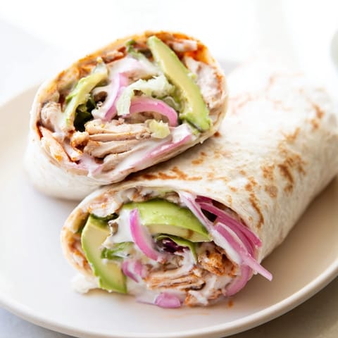 Sliced Smoky Chipotle Chicken Wrap halves showing juicy marinated chicken, bright green lettuce, and rich avocado with a dollop of creamy Greek yogurt sauce on a rustic plate.