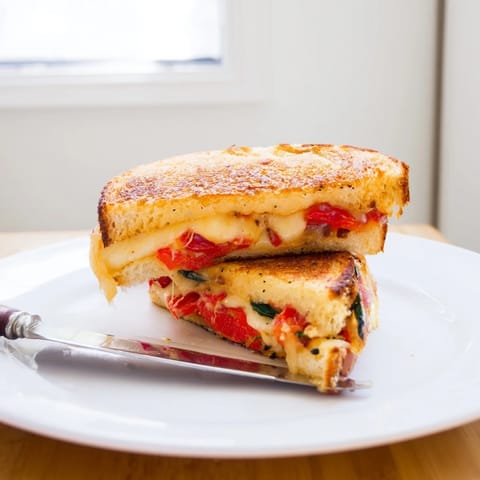 A close-up of a sliced Pepper Jack & Tomato Grilled Cheese reveals oozing, creamy pepper jack cheese layered with juicy red tomato on buttery, grilled bread.