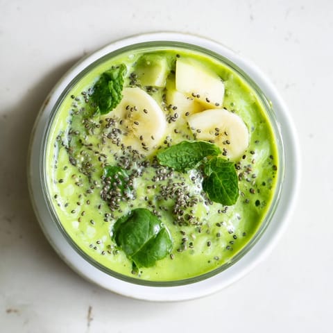 A frothy glass of green detox smoothie garnished with mint, ready to sip beside fresh lemon wedges and apple slices.  