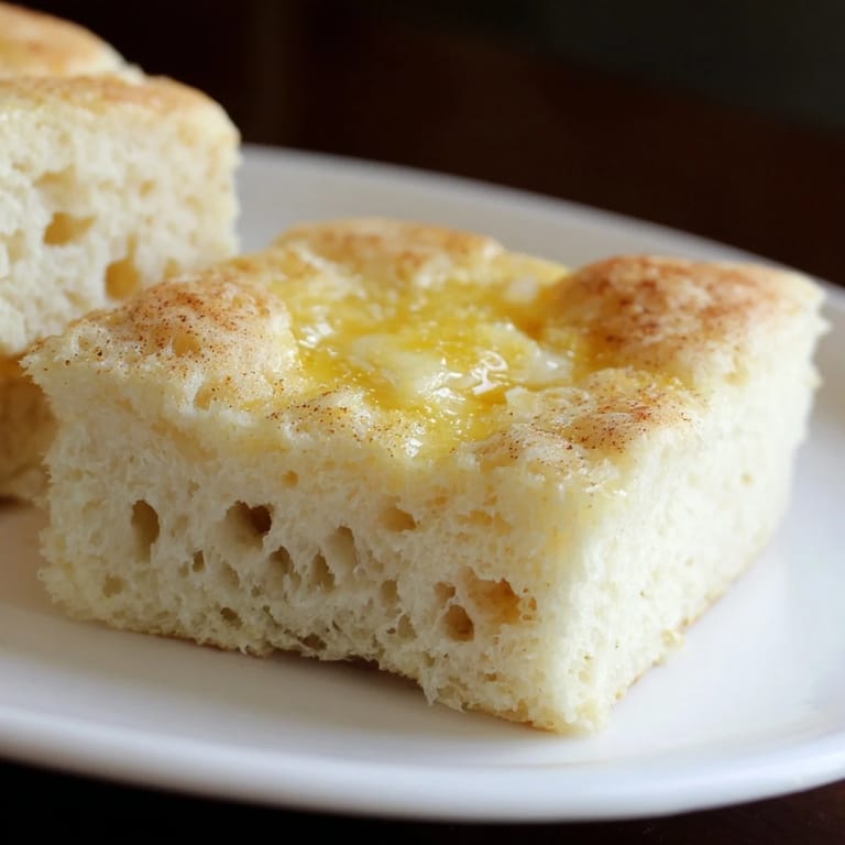 A close-up of freshly baked sheet pan English muffins with a dusting of cornmeal.