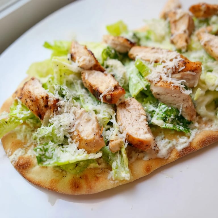 Savory Chicken Caesar Flatbread arranged on a white plate with romaine lettuce, Caesar drizzle, and herbs, perfect for a light lunch or shareable snack.