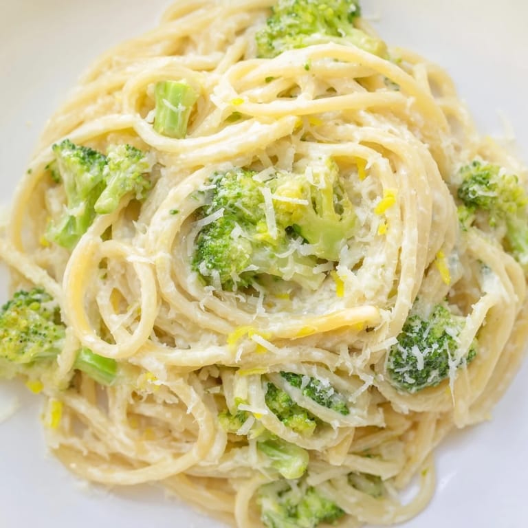 Garlic-infused sauce clings to spaghetti and broccoli in a deep skillet, topped with basil and extra Parmesan for serving.