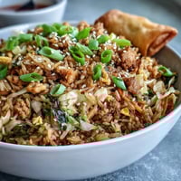 Crispy Chicken Fried Rice with Egg Roll Flavors served hot, garnished with green onions and sesame seeds on a plate.